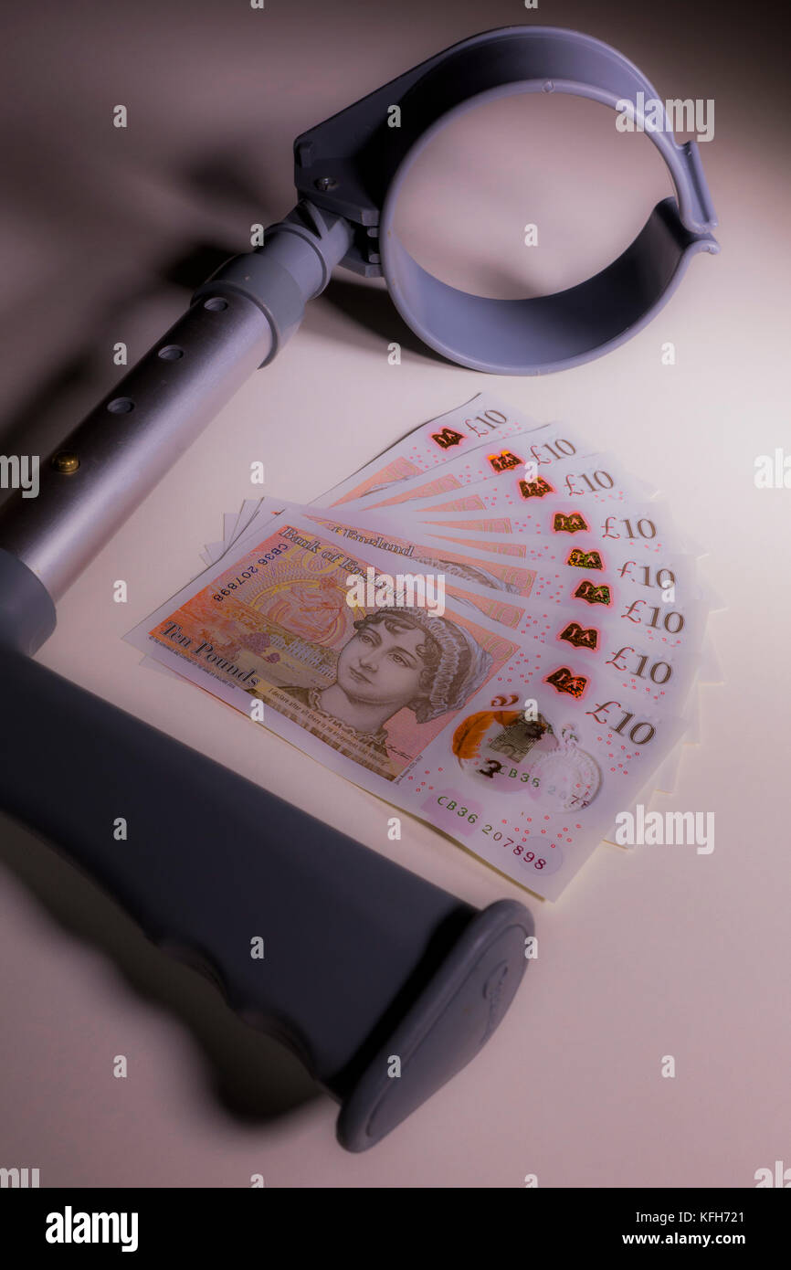 Crutch and new polymer sterling £10 ten pound notes. Concept of link between incapacity and UK pounds, such as disability income and healthcare cost. Stock Photo