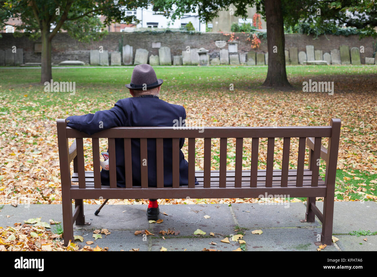 Old man sitting on bench in grounds of St George's Deal church with gravestones around perimeter, Deal, Kent, England, United Kingdom, Europe Stock Photo