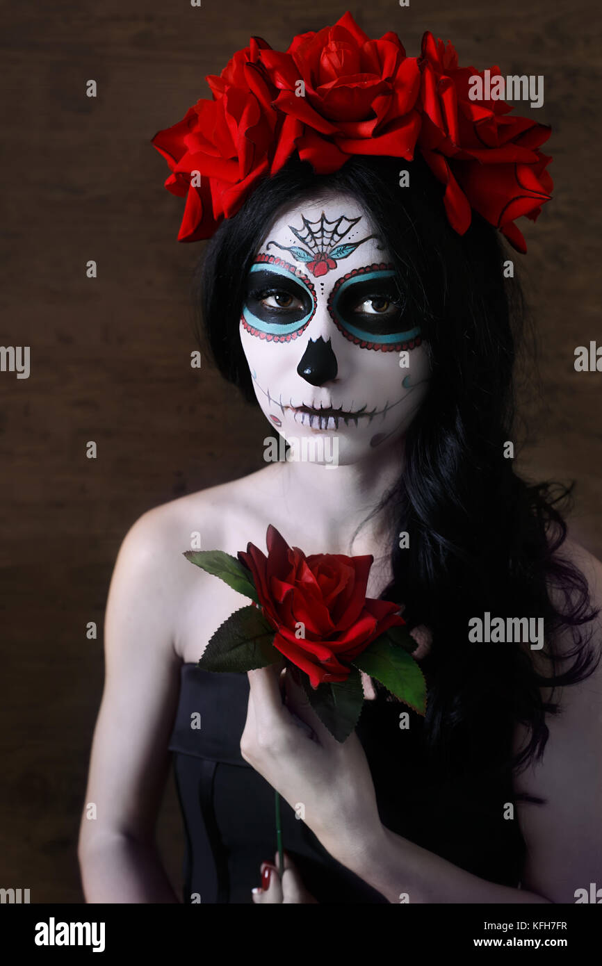 Day of the dead. Halloween. Young woman in day of the dead mask skull face art and rose. Dark background. Stock Photo
