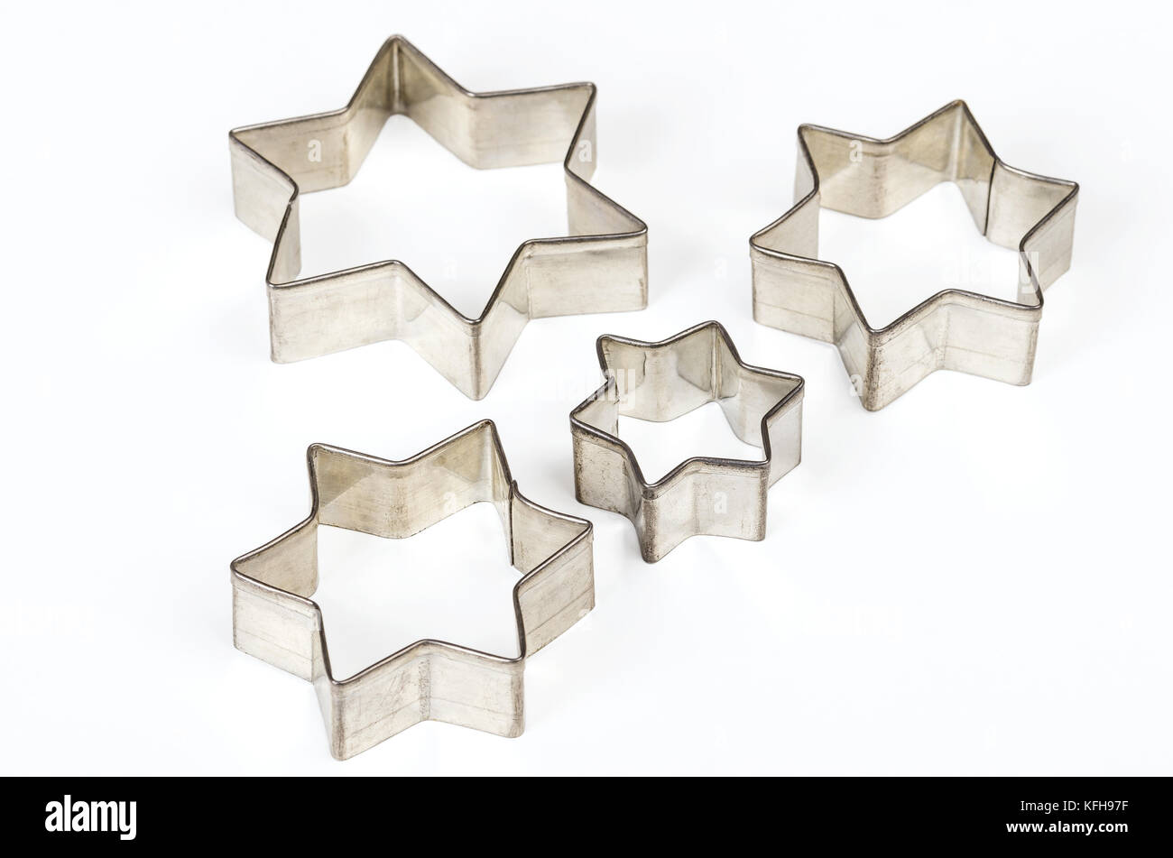 Four star shaped Christmas cookie cutters over white. Tin biscuit cutters, tool to cut cookie dough in particular shapes and to make cutouts. Stock Photo