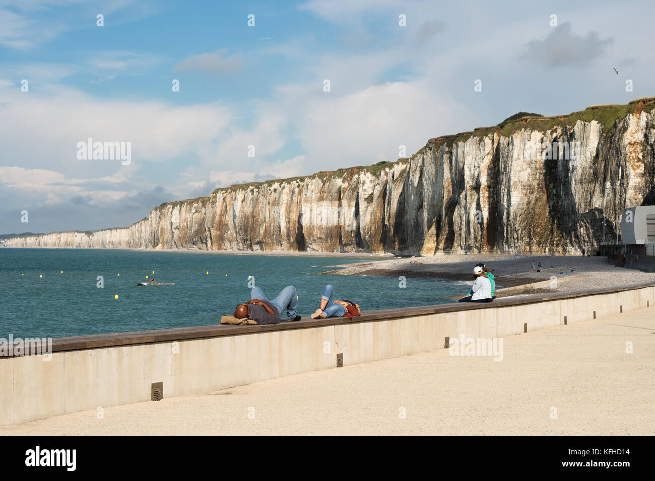 Couple lying on harbour wall with white limestone cliffs in background, Saint Valery en Caux, Normandy, France, Europe Stock Photo