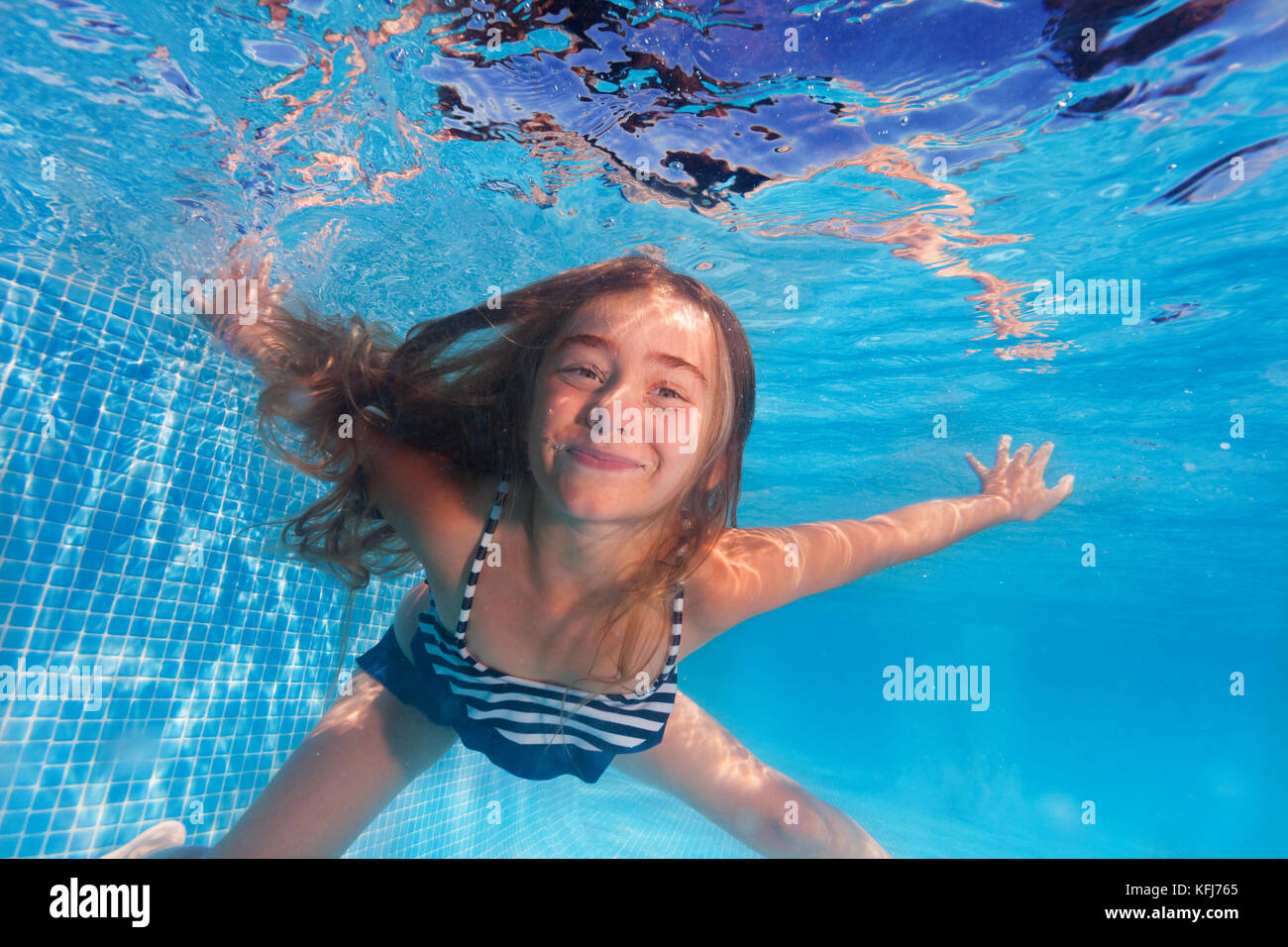 Underwater shoot of cute girl diving under clear water of swimming pool