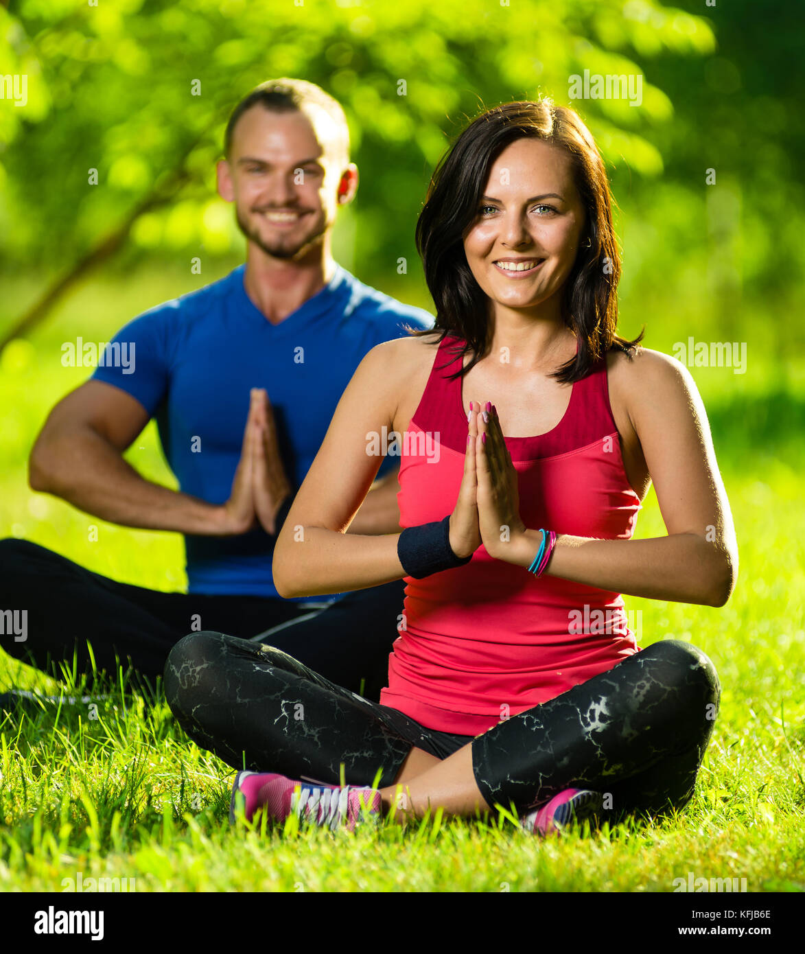 Young man and woman doing yoga in the sunny summer park Stock Photo