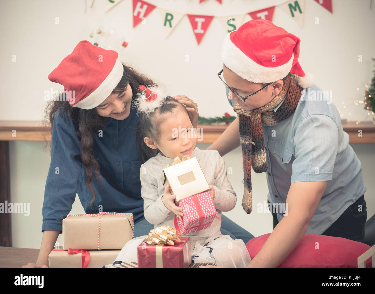 Happy family Asia family wear santa claus hat unwrap Christmas gift box at house xmas party,Holiday celebrating festive concept,vintage filter Stock Photo