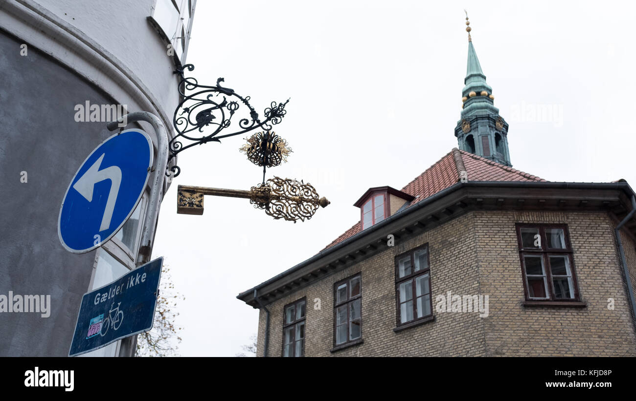 Locksmith's hanging sign in the Latin area of Copenhagen, Denmark with the Sankt Petri Kirche steeple in the background. Stock Photo