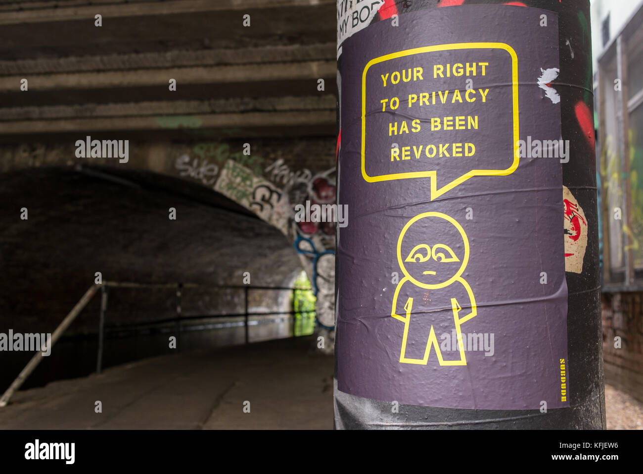 Street art poster hung on column near a tunnel from artist SUBDUDE with stylised man and cartoon with slogan 'Your right to privacy has been revoked'. Stock Photo