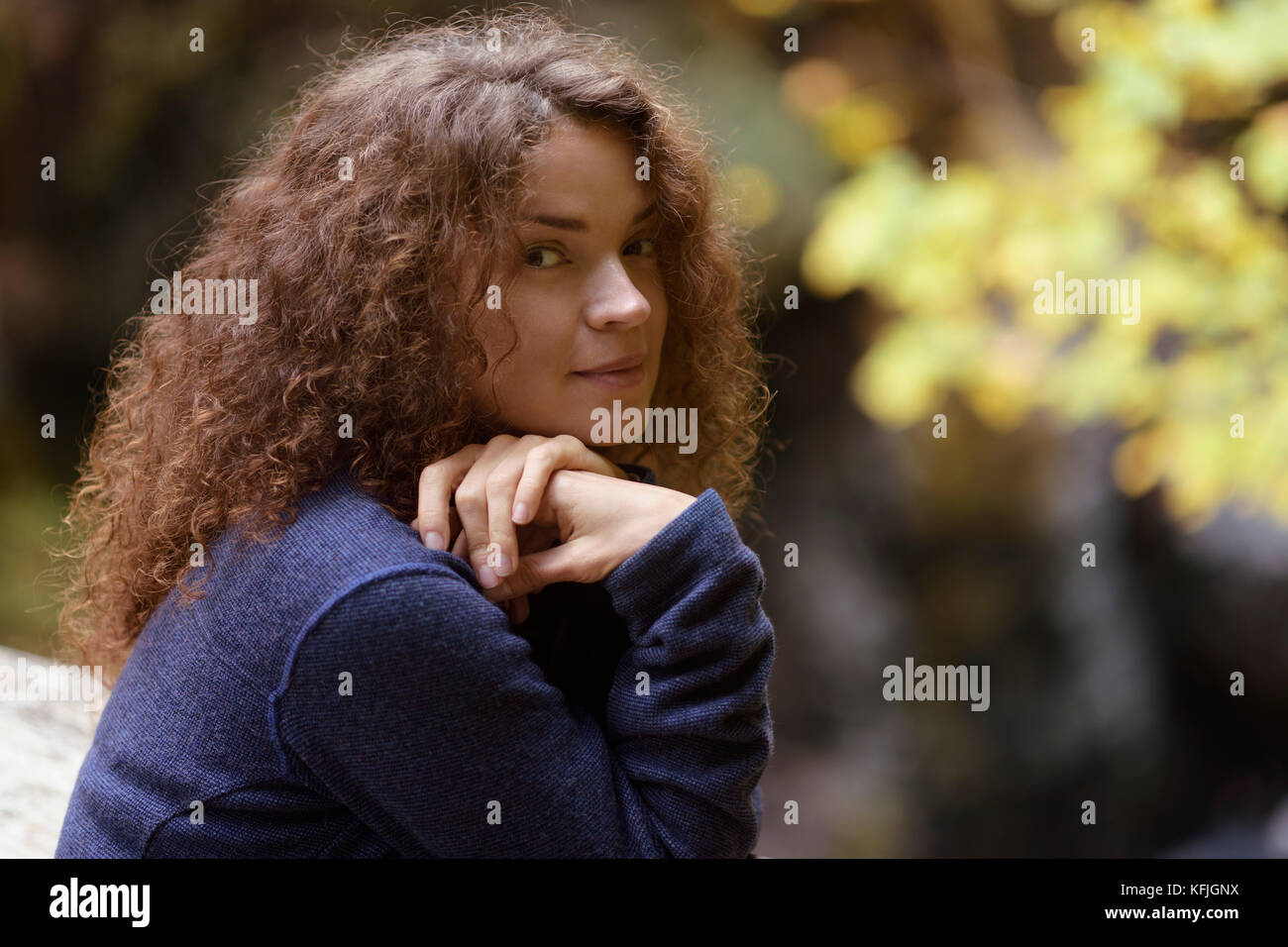 Candid natural portrait of a young woman with long brown hair and cute smiling expression on her face in fall nature scenery Stock Photo