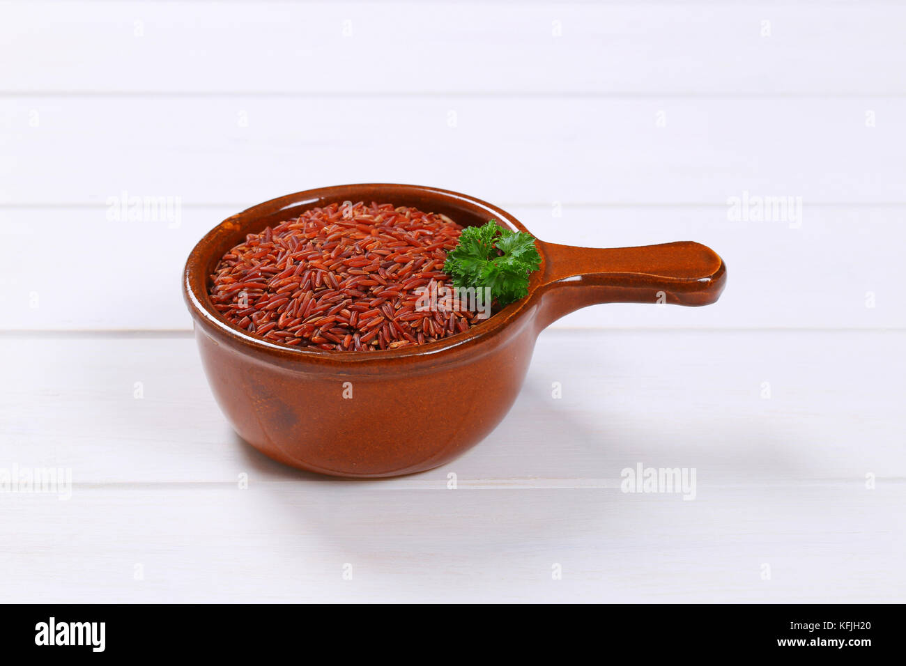 saucepan of red rice on white wooden background Stock Photo