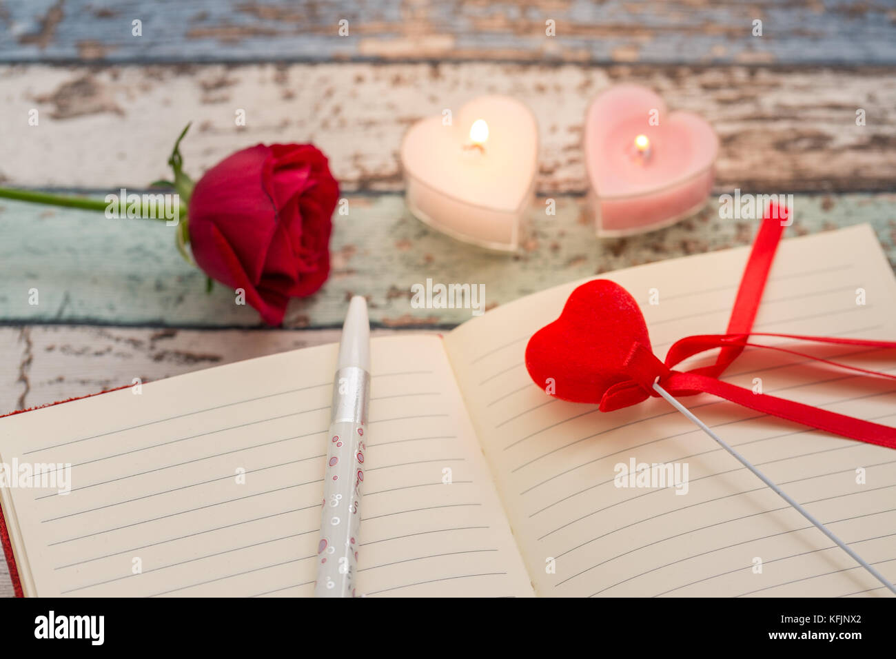 Writing for love: red rose, journal and pen with candles Stock Photo