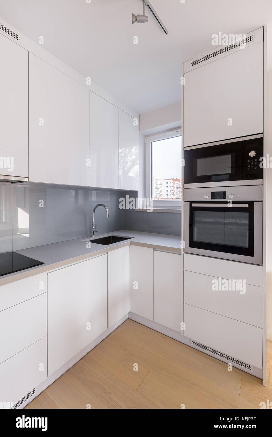 Small, white kitchen with gray wall tiles and wooden floor Stock Photo -  Alamy