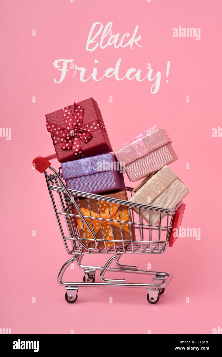 a shopping cart full of gifts of different colors and the text black friday on a pink background Stock Photo