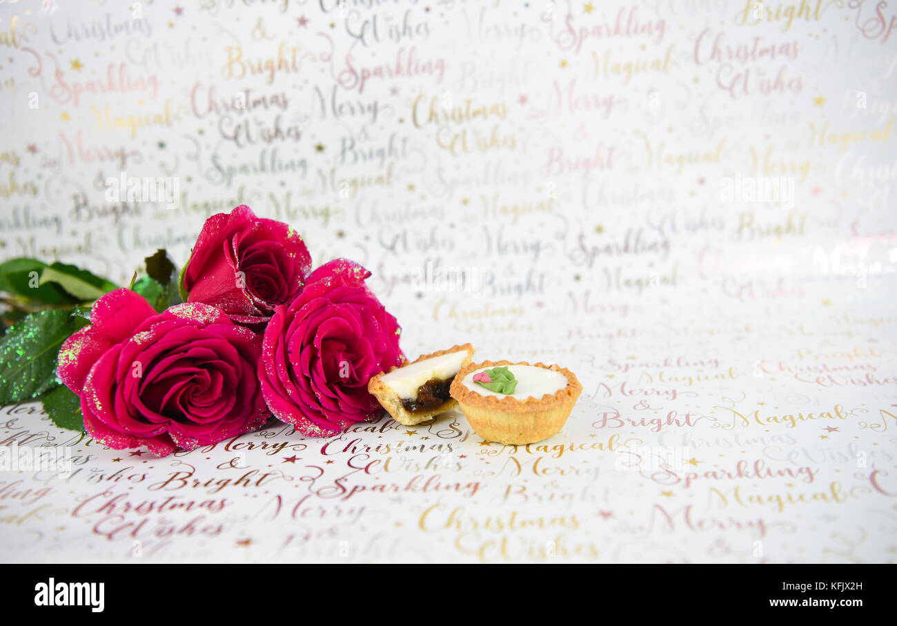 Christmas food photography image with xmas glitter red roses and iced mince pies on white shiny wrapping paper background with festive writing Stock Photo