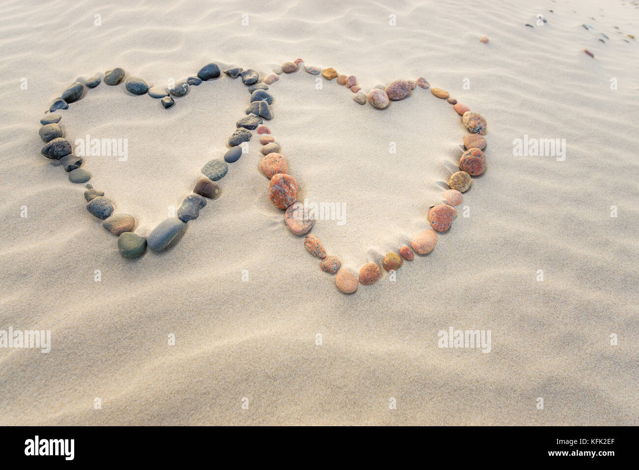 Pebbles arranged in shape of two hearts on sand beach ripples Stock Photo