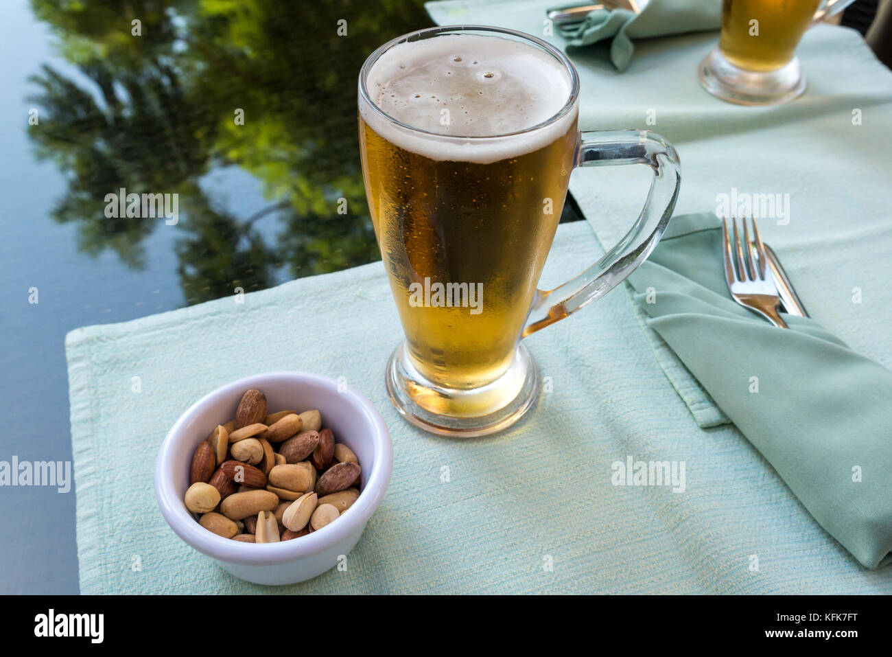 Close up of cold beer glass mugs and mixed nuts in small dish on glass