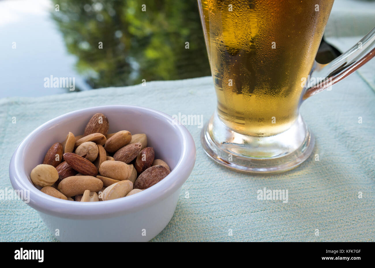 Close up of cold beer glass mug and mixed nuts in small dish on lunch table setting with blurred background, Jordan, Middle East Stock Photo