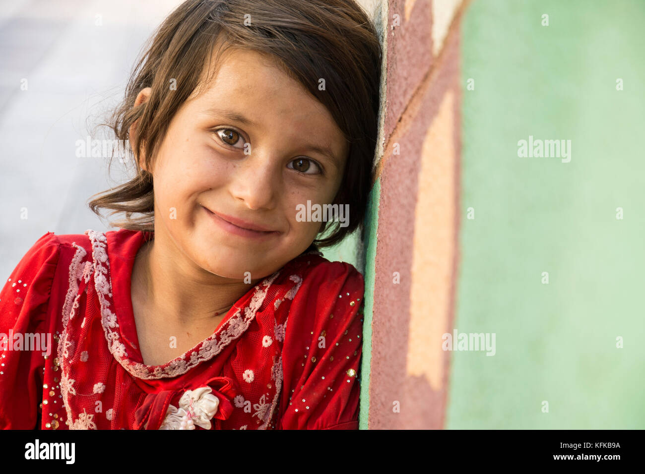 Tehran, IRAN - August 16, 2017  Close up portrait of a lonely  little girl selling small tissue packages at street pavement in front of painted wall Stock Photo