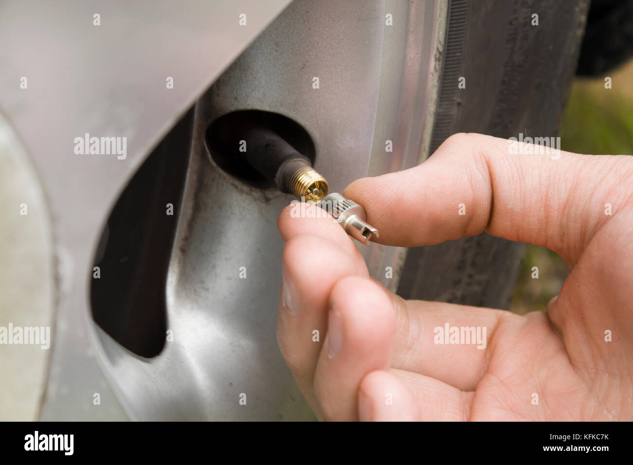 The mechanic's hand unscrews the valve cap in the wheel of the car. Stock Photo