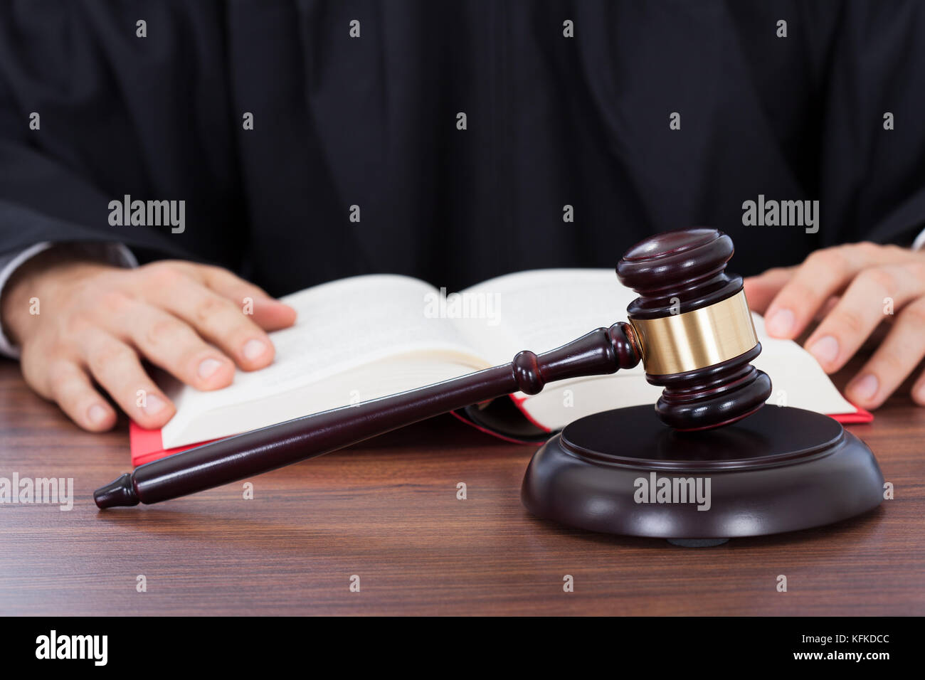 Closeup of gavel placed on block with judge reading law book at desk Stock Photo