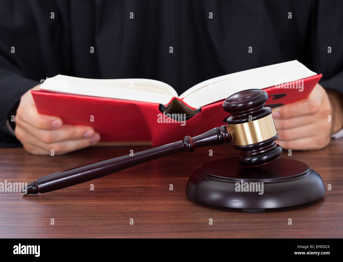 Closeup of gavel placed on block with judge reading law book at desk Stock Photo