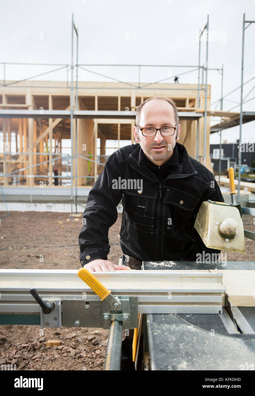 Confident Mature Carpenter Using Table Saw To Cut Plank Stock Photo