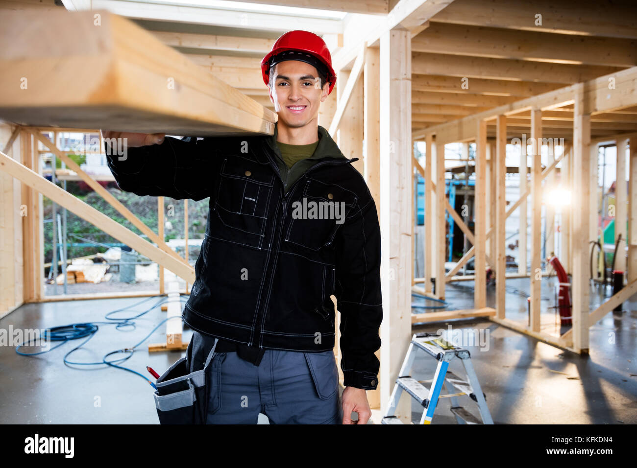 Smiling Male Carpenter Carrying Wood At Construction Site Stock Photo