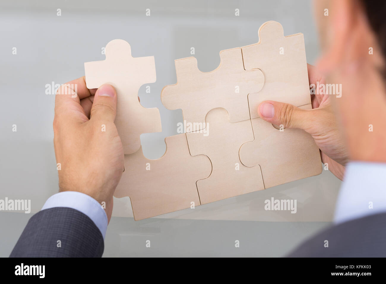 Businessman assembling jigsaw puzzle. Over the shoulder view Stock Photo