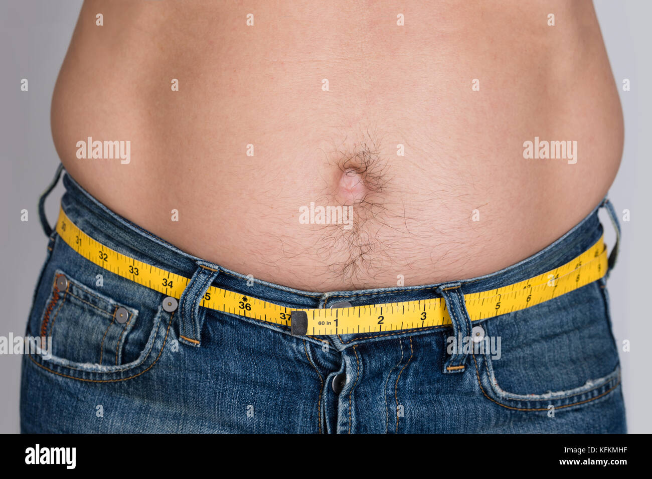 Closeup midsection of man with measure tape around waist against gray background Stock Photo