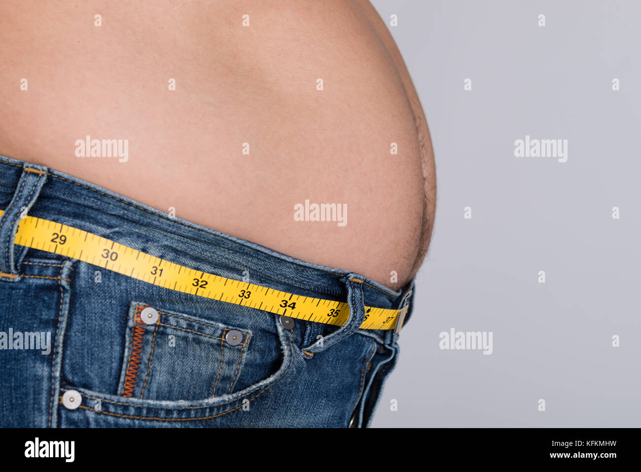 Side view midsection of fat man with measure tape around waist against gray background Stock Photo