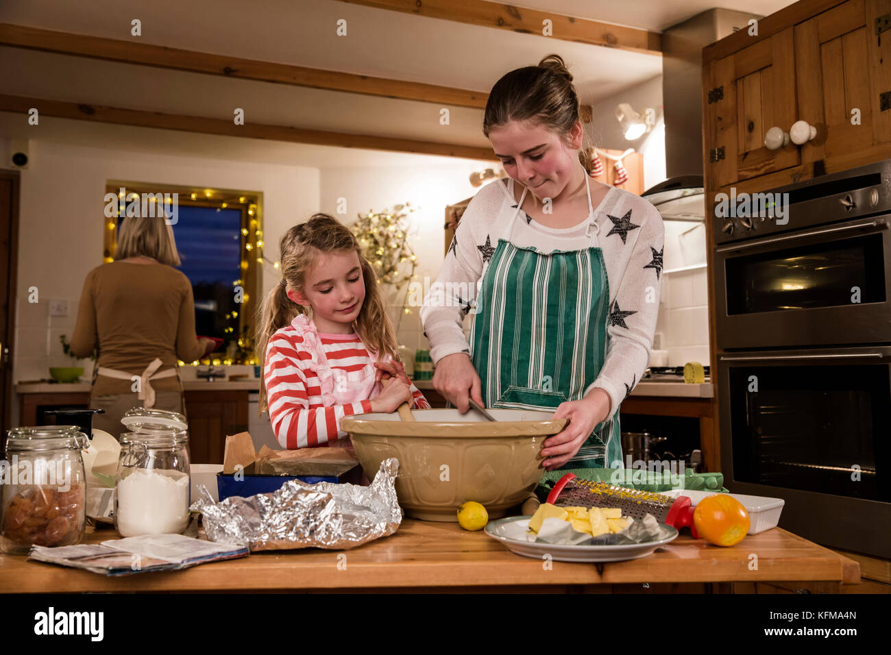 Two sisters are baking cakes in the kitchen with their grandmother. The girls are mixing ingredients. Stock Photo