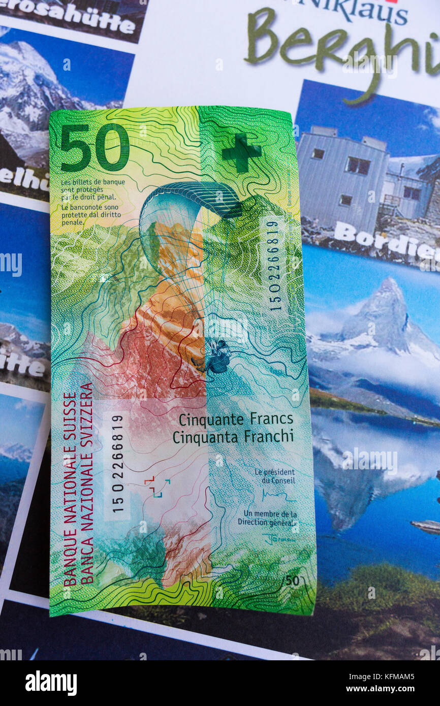 ST. NIKLAUS, SWITZERLAND - Swiss franc note with image of paraglider, 50 CHF, in front of tourism guide. Stock Photo