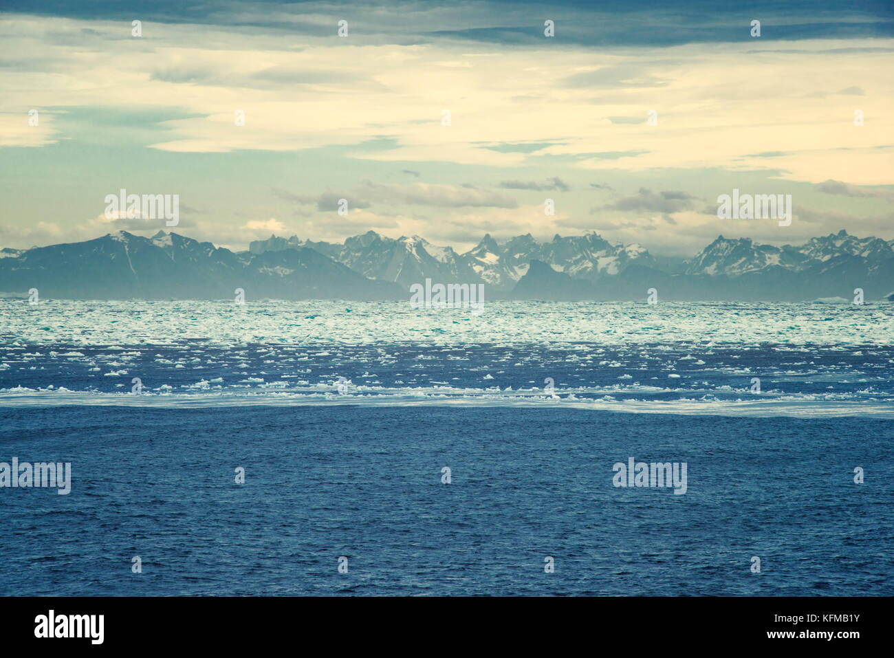 Sunrise over Greenland. High mountain range surrounded by icy waters at ...