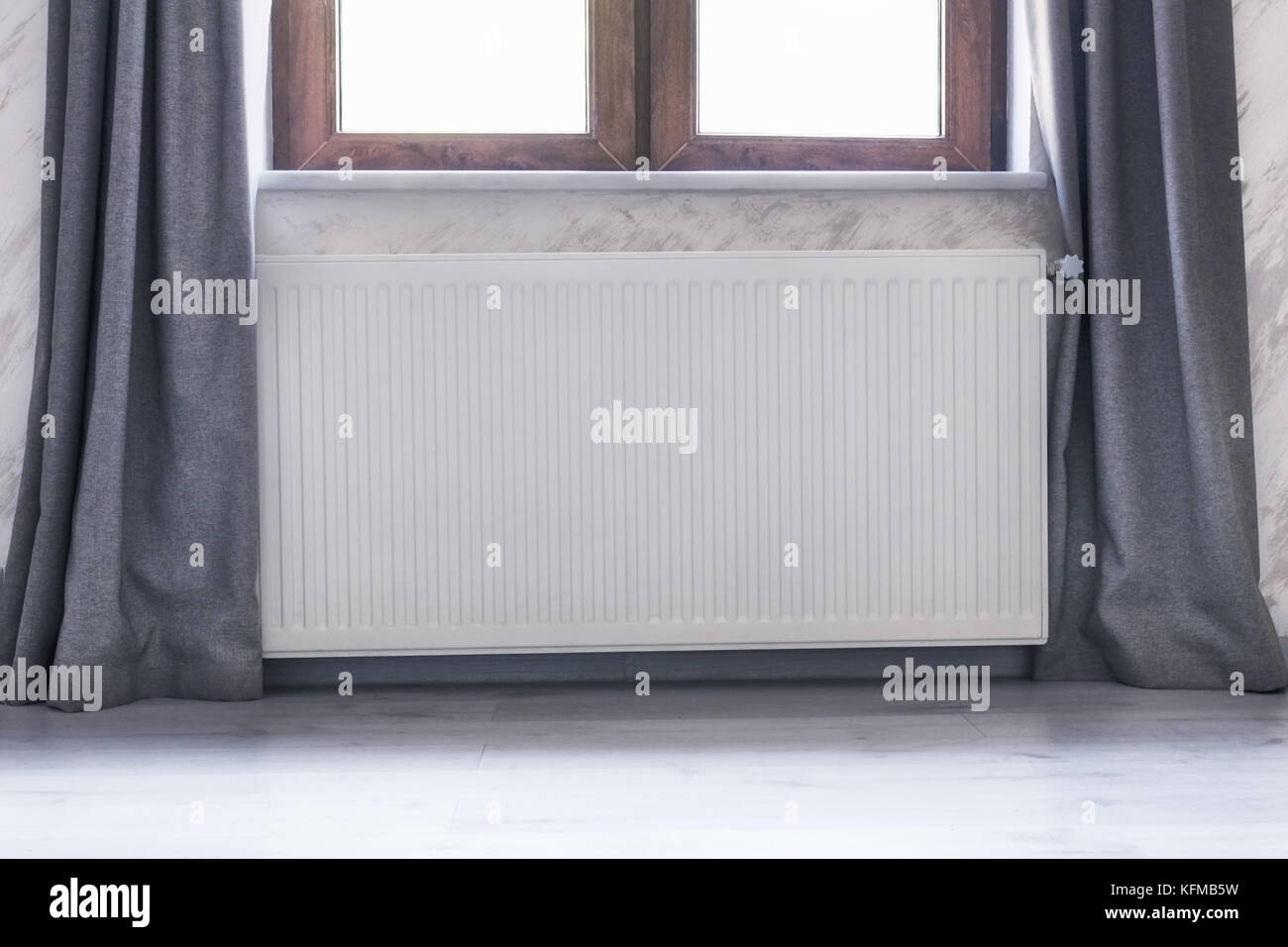 Heating radiator under the window with a wooden frame and curtains