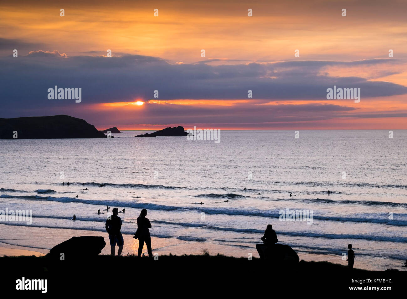 Spectacular sunset - people seen in silhouette as they watch the sun setting over The Goose and East Pentire Headland in Newquay Cornwall. Stock Photo