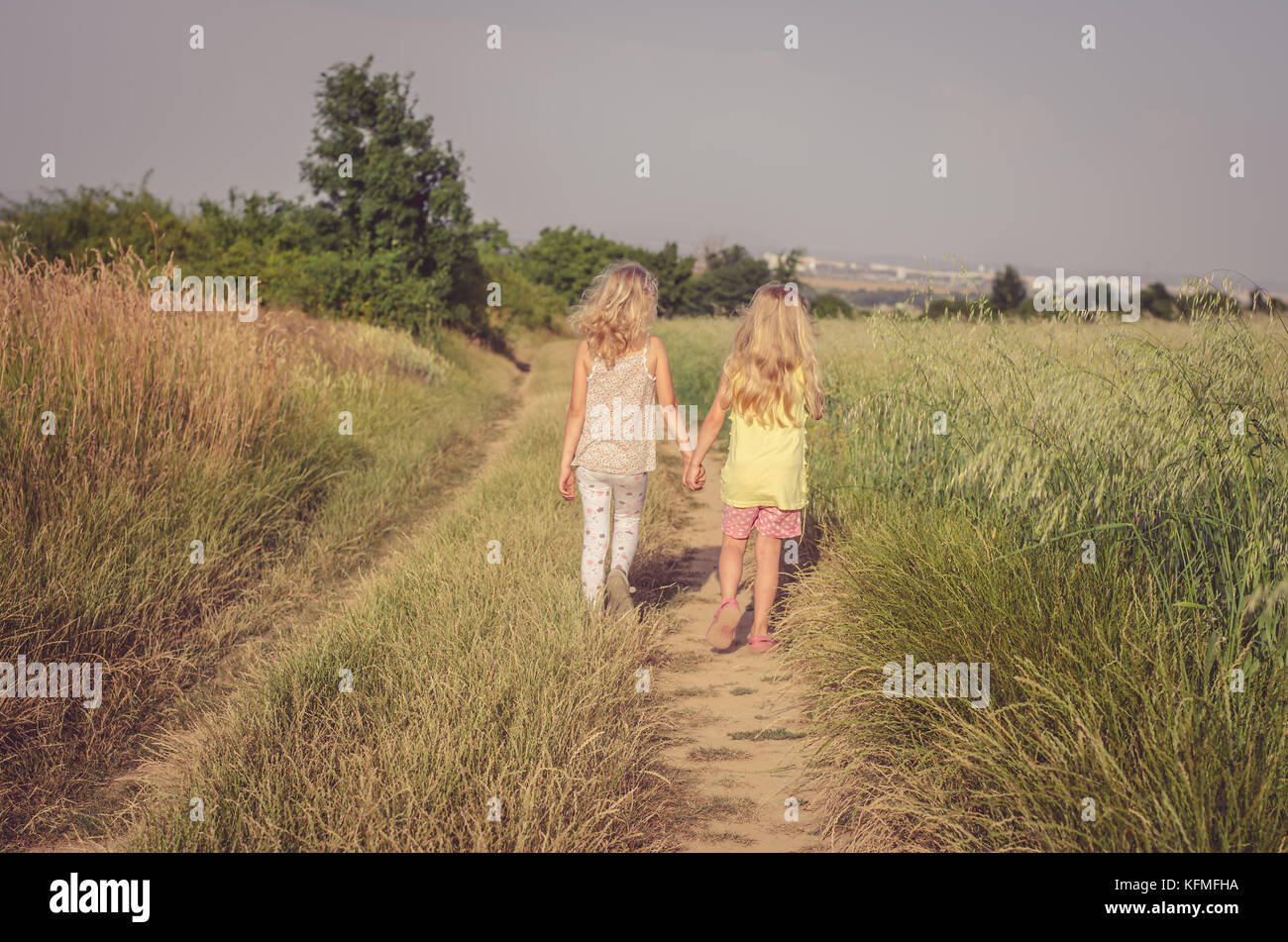 two children walking in romantic colorful rural path among fields Stock Photo