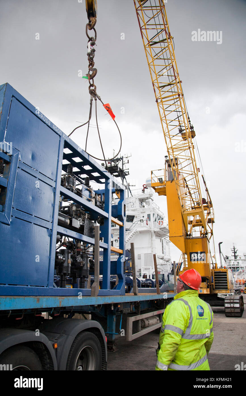 Asco Offshore crane lifting equipment from flatbed trailer onto ship in
