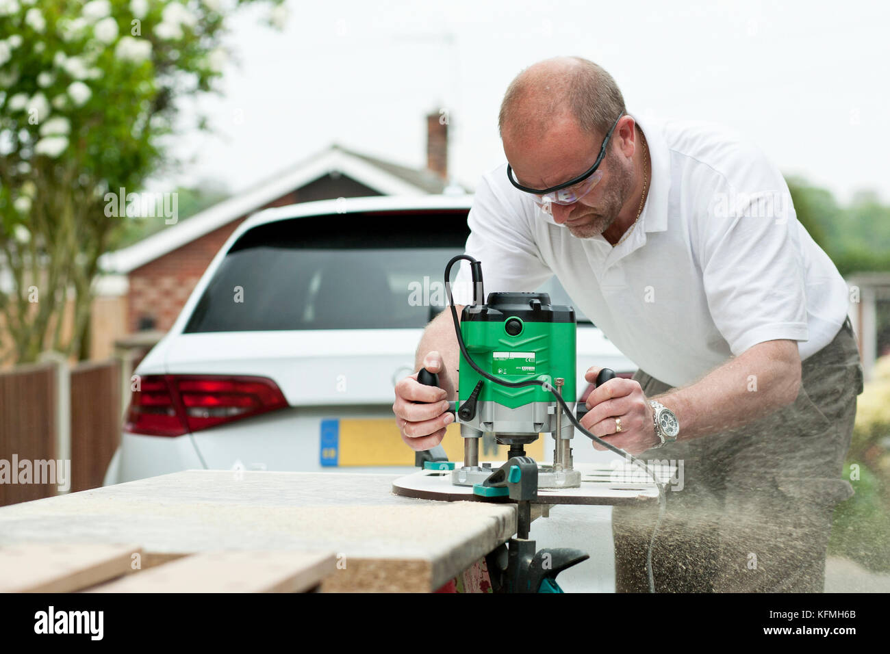 Man cutting kitchen unit top outside residential property using a wood router. Stock Photo