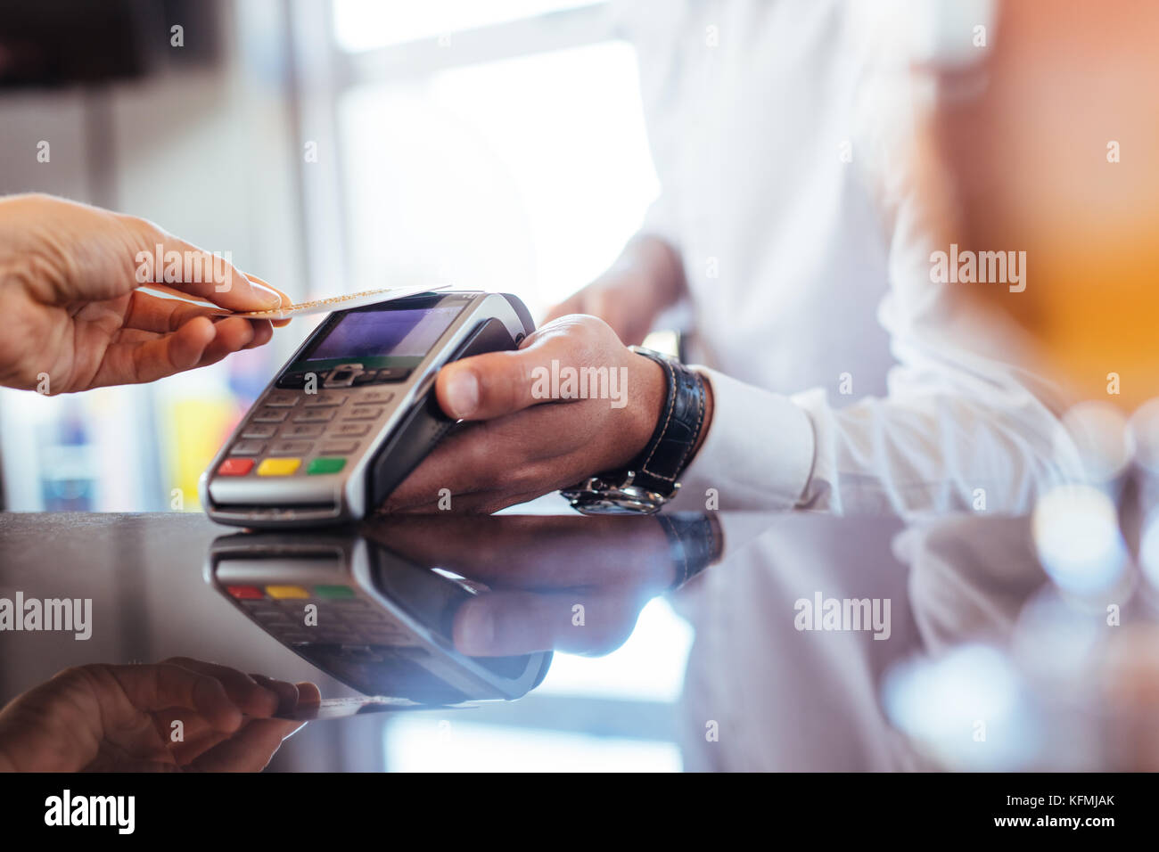 Hand of customer paying with contactless credit card with NFC technology. Bartender with a credit card reader machine at bar counter with female holdi Stock Photo