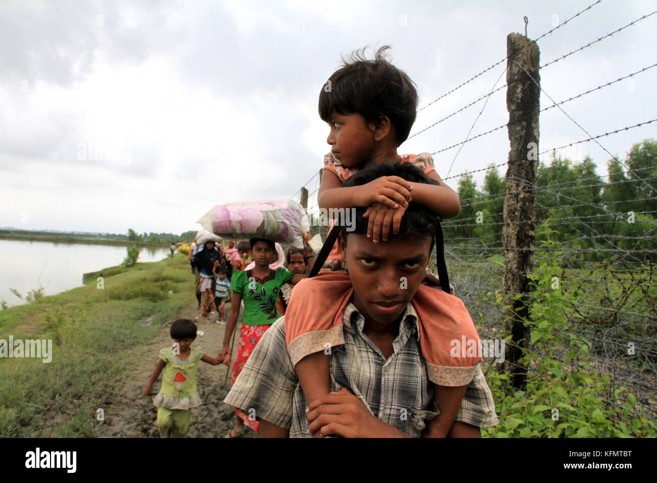 Myanmar: Rohingya refugees fleeing military operation in Myanmar’s Rakhine state, walk along the Myanmar-Bangladesh border fence near Maungdaw to take shelter into Bangladesh on September 7, 2017. Over half a million Rohingya refugees from Myanmar’s Rakhine state, have crosses into Bangladesh since August 25, 2017 according to UN. The Myanmar military's latest campaign against the Rohingyas began after the attack on multiple police posts in Rakhine state. © Rehman Asad/Alamy Stock Photo Stock Photo