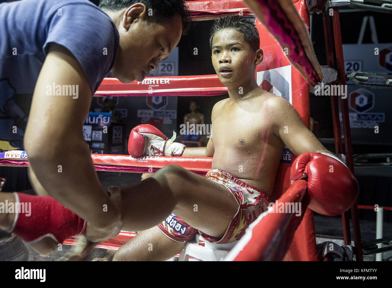 Young Thai boxing sitting in the conner of the ring, attended by his ...