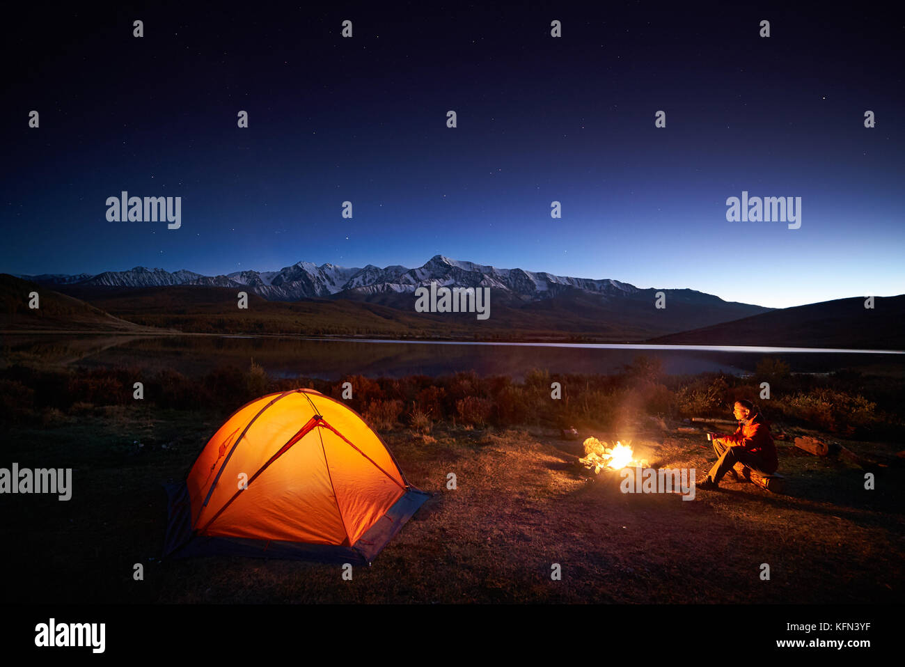 Man tourists sitting in the illuminated tent near campfire Stock Photo