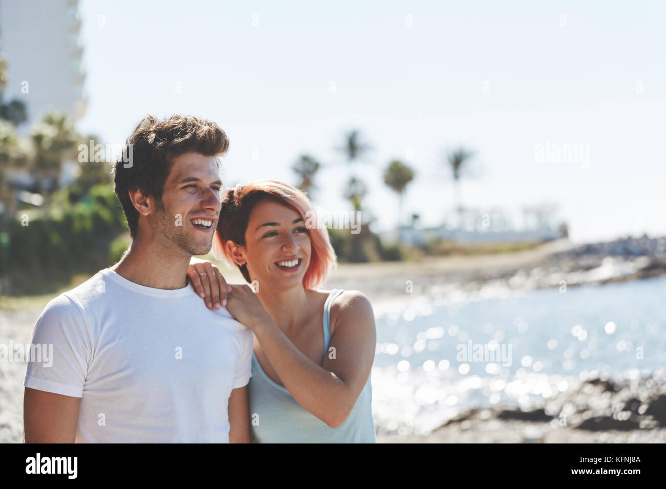 Portrait of happy couple standing together on beach looking away Stock Photo