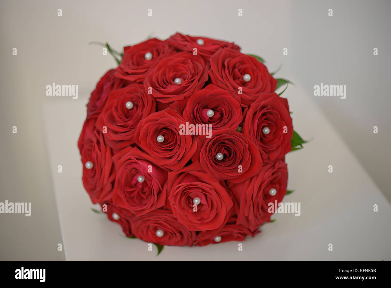 Sophisticated round wedding bouquet with red roses and pearl drops positioned on a white minimalist table Stock Photo