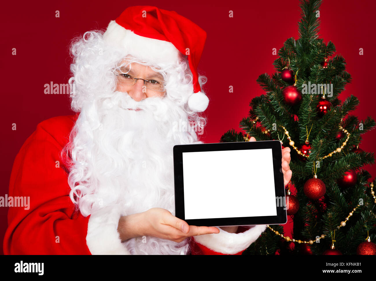 Portrait of a happy santa holding digital tablet over red background ...
