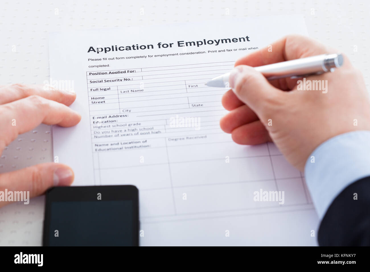 Close-up Of Hand Holding Pen Over Employment Application With Mobile Phone Stock Photo