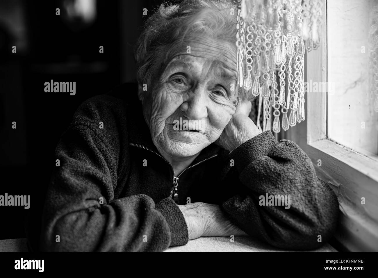 Sad elderly woman sitting near the window. Black-and-white photo. Stock Photo