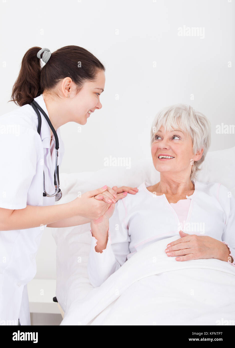 Happy Young Female Doctor With Hand On Senior Female Patient Stock Photo