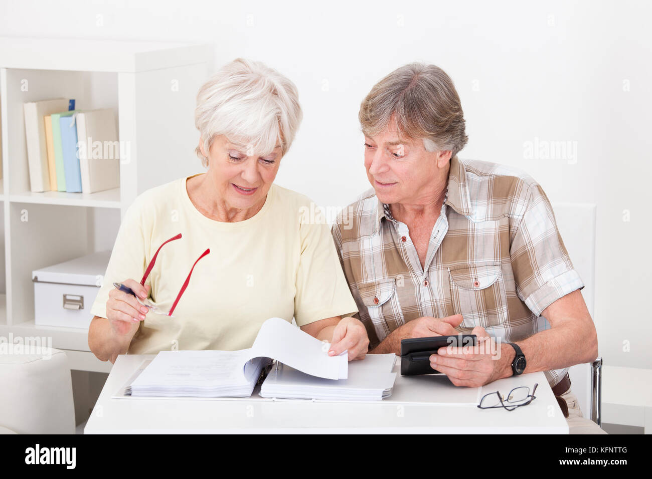 Elderly Woman Checking The Accounts While The Husband Adds Up The Figures On The Calculator Stock Photo