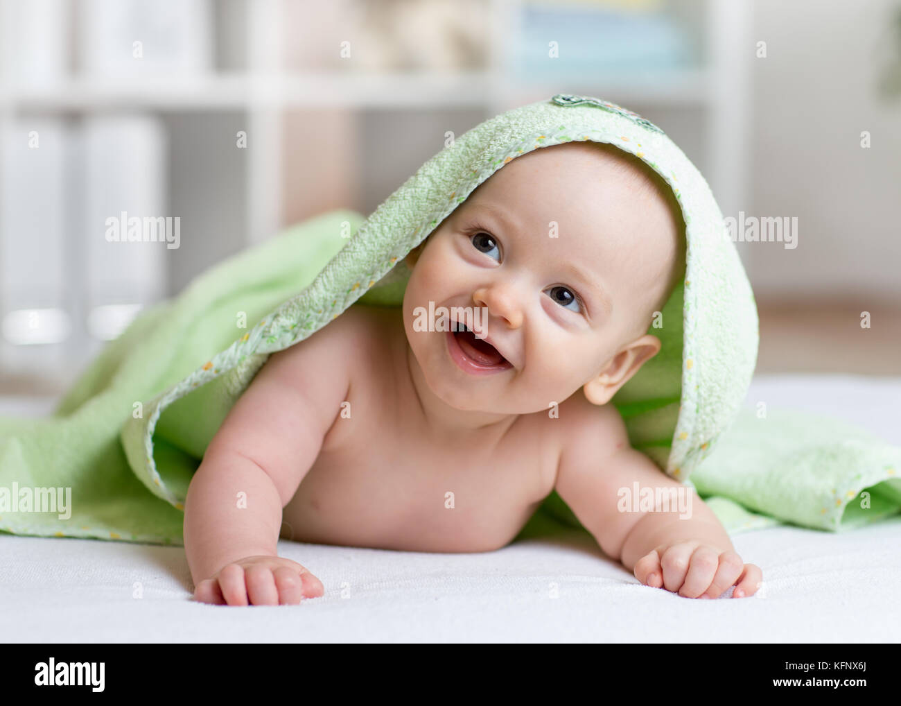 Portrait Of Adorable Smiling Baby In Hooded Towel Lying On Bed After Having Bathtime Stock Photo