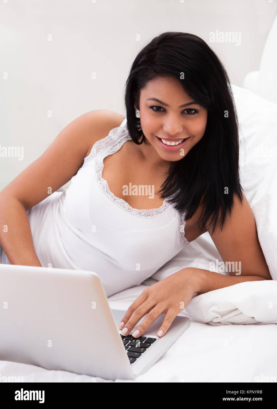 Portrait Of Young Woman Lying On Bed And Using A Laptop Stock Photo