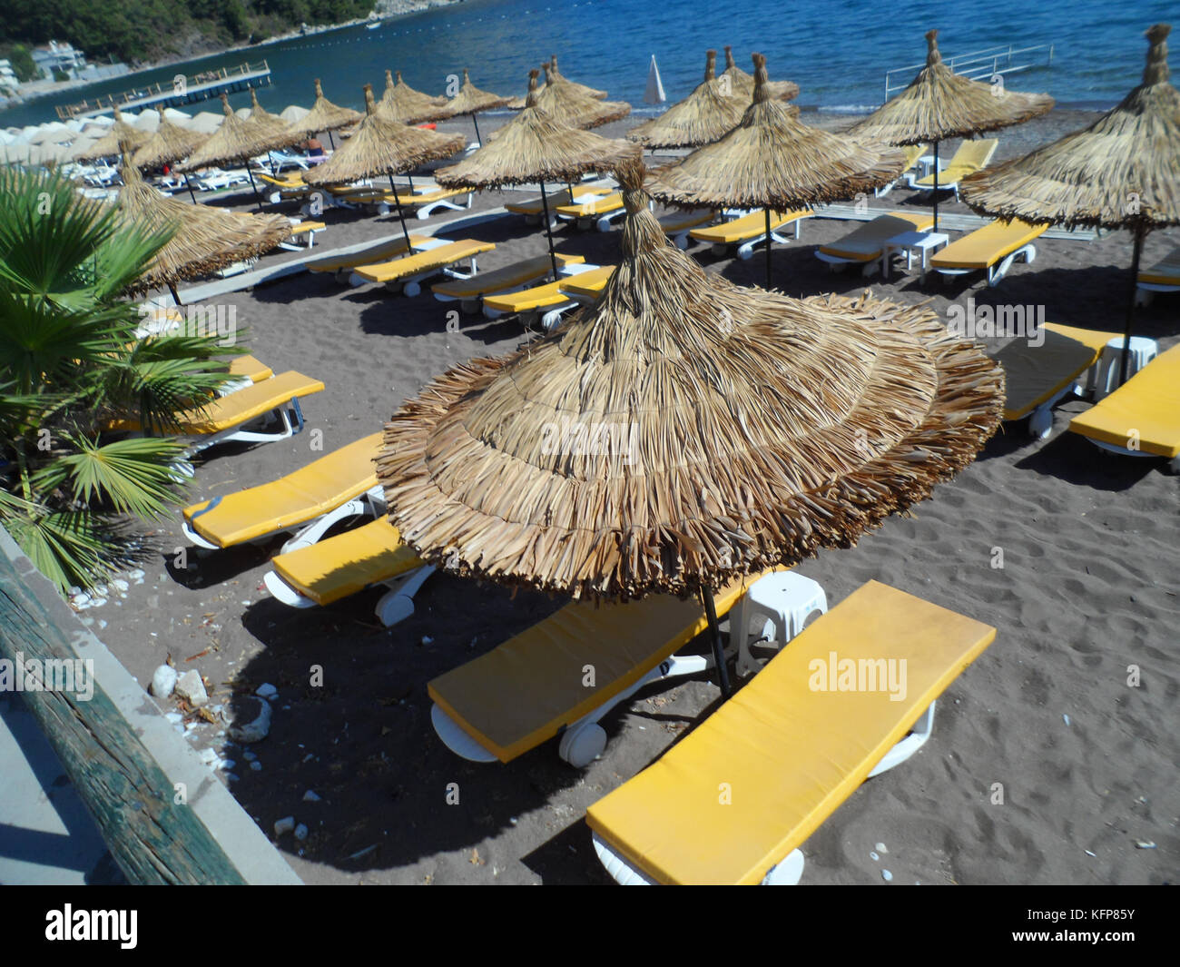 Wicker sunshade parasols and sun loungers on the public beach at Turunc, Turkey, Europe. Stock Photo